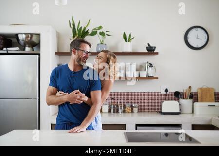 Come fare colazione, amore mio. una felice coppia di mezza età che si abbraccia in cucina a casa. Foto Stock