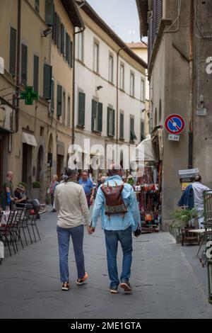 Coppia di mezza età (uomo e donna) con le mani che camminano lungo via Nazionale a Cortona, Toscana, Italia. Foto Stock