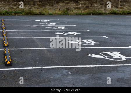 Una fila di vani auto per la ricarica di veicoli elettrici. Le baie mostrano il simbolo ufficiale del Dipartimento dei Trasporti per un'auto elettrica dipinta sul asfalto. Foto Stock