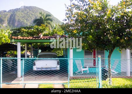 Piccola casa verde con auto retrò parcheggiata vicino a alberi tropicali e montagna in giornata di sole a Cuba Foto Stock
