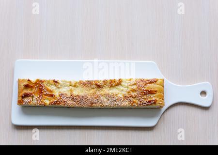 tagliere di porcellana bianca grande pezzo di strudel di torta con casetta formaggio casseruola cosparsa di semi di sesamo fresco spazio pasticceria per il testo sul morbido tavolo ristorante rosa che serve fatto in casa Foto Stock