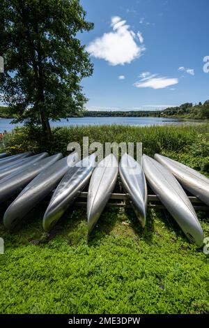 Mölndal, Svezia - Luglio 17 2022: Lunga fila di canoe metalliche rovesciate da un lago Foto Stock