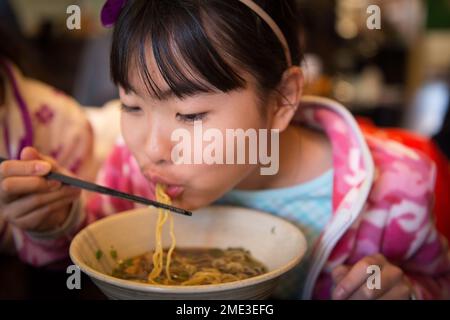 Ragazza asiatica che mangia ramen in un ristorante locale Foto Stock