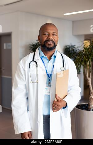 Ritratto verticale di felice medico afro-americano maschio nel corridoio dell'ospedale Foto Stock