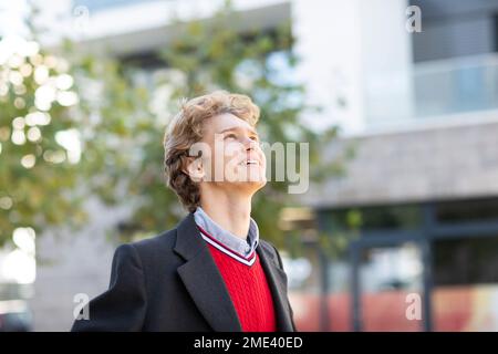 Felice giovane uomo con i capelli biondi che indossano il pullover rosso e la giacca Foto Stock