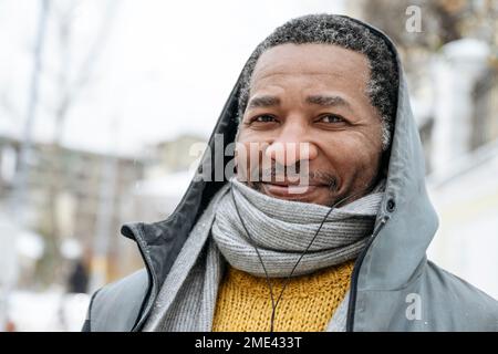 Uomo sorridente che indossa abiti caldi e ascolta la musica con le cuffie intrauricolari Foto Stock