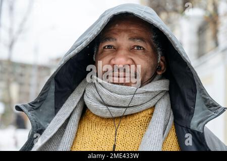 Uomo maturo che indossa abiti caldi e ascolta la musica con le cuffie intrauricolari Foto Stock