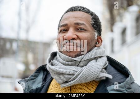 Uomo maturo sorridente che indossa abiti caldi e ascolta la musica con le cuffie intrauricolari Foto Stock