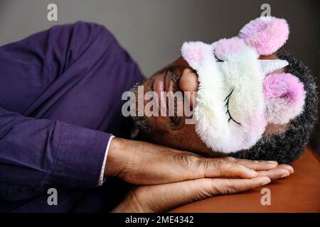 Uomo maturo che indossa una maschera oculare unicorno che dorme a letto Foto Stock