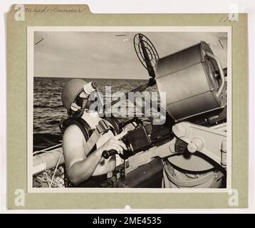 Gunner mascherato. Questa immagine raffigura un artigliere della Guardia Costiera, che indossa un casco e una maschera a gas, seguendo il corso di un aereo sospeso durante un'esercitazione. Foto Stock