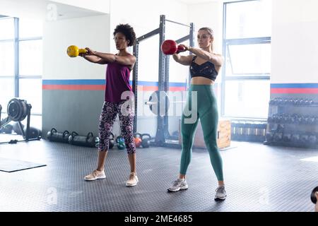 Diverse donne in forma che si allenano e utilizzano le campane di un kettlebells in palestra Foto Stock
