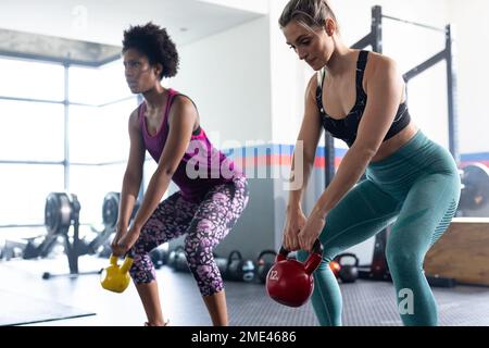 Diverse donne in forma che si allenano e utilizzano le campane di un kettlebells in palestra Foto Stock