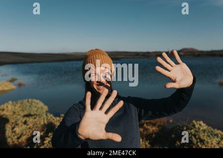 Donna sorridente che protegge gli occhi dalla luce del sole al lago Foto Stock