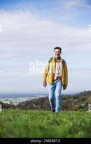 Uomo sorridente che cammina con lo zaino sull'erba Foto Stock