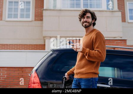Felice giovane uomo che ricarica l'auto di fronte all'edificio Foto Stock