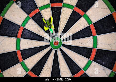 Singola freccetta nera e verde bloccata nel bullseye di una freccetta. Primo piano di una tavola da disegno. Foto Stock