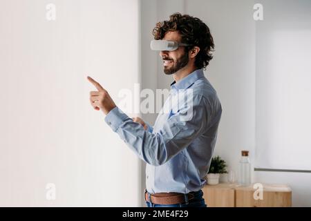 Uomo d'affari che indossa occhiali VR a contatto con lo schermo trasparente in ufficio Foto Stock