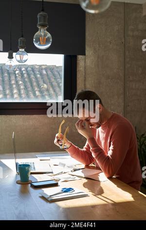 Uomo stanco seduto alla scrivania con bollette finanziarie a casa Foto Stock