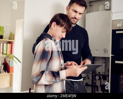 Figlio e padre su una caldaia digitale di controllo tablet per il risparmio energetico a casa Foto Stock