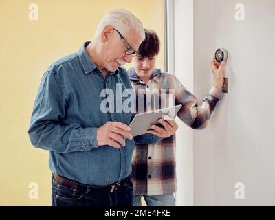 Nonno e nipote che guardano il termostato intelligente sul tablet digitale a casa Foto Stock