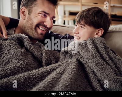 Felice padre e figlio che si snuggling sotto una coperta sul divano in soggiorno Foto Stock