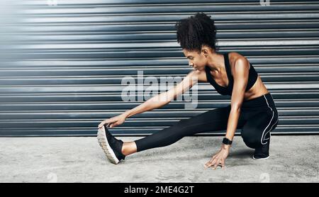 Rialzarsi. una giovane donna sportiva che allunga le gambe su uno sfondo grigio. Foto Stock