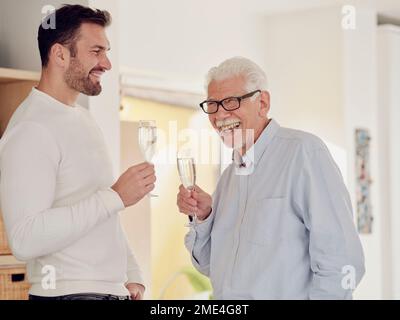 Un uomo anziano e un figlio adulto festeggiano a casa brindando con champagne Foto Stock