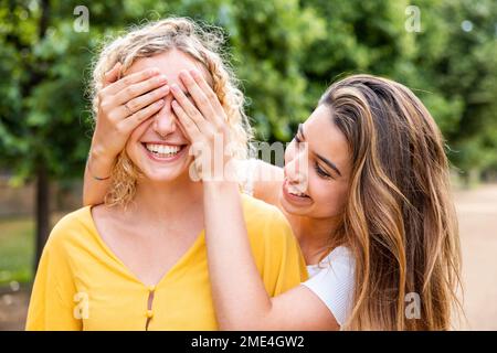 Donna sorridente che copre gli occhi dell'amico con le mani nel parco Foto Stock