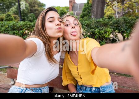 Amici che fanno i volti e che prendono selfie sulla panchina nel parco Foto Stock