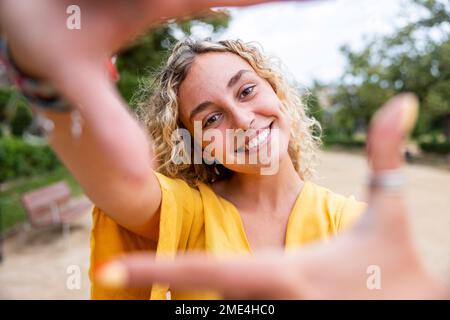 Felice giovane donna che fa la cornice del dito nel parco Foto Stock