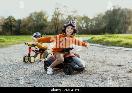 Ragazzo sorridente seduto con le braccia tese su bobby auto con il fratello sullo sfondo Foto Stock