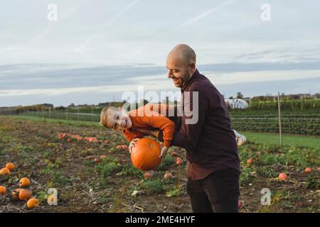 Padre che porta il figlio che tiene la zucca in campo Foto Stock