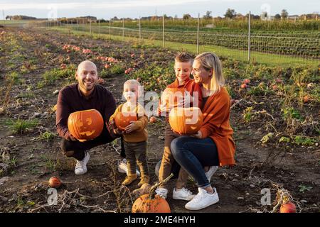 Genitori felici con bambini che tengono jack o' lanterne in campo Foto Stock