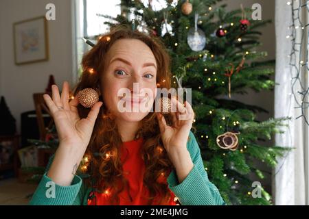 Donna sorridente con orecchini davanti all'albero di Natale Foto Stock