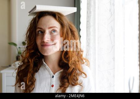 Donna sorridente libro di bilanciamento in testa a casa Foto Stock