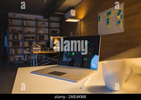 Diagramma e dati sullo schermo del laptop alla scrivania in ufficio Foto Stock