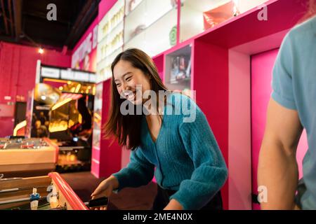 Felice giovane donna che gioca a calcio da tavolo nella sala giochi Foto Stock