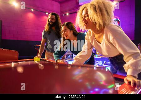 Amici felici che si divertono a giocare a hockey su ghiaccio nella sala giochi Foto Stock