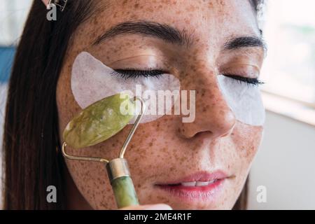 Donna con il viso increckle massaggiante con rullo di pietra di giada Foto Stock