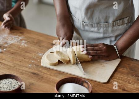 Primo piano della donna nera che cuoce pasta fatta in casa sul banco della cucina in legno scuro, spazio copia Foto Stock