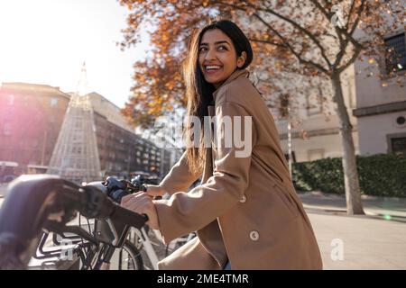 Giovane donna sorridente che noleggia una bicicletta nelle giornate di sole Foto Stock