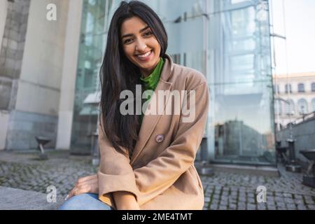 Felice giovane donna seduta fuori edificio Foto Stock