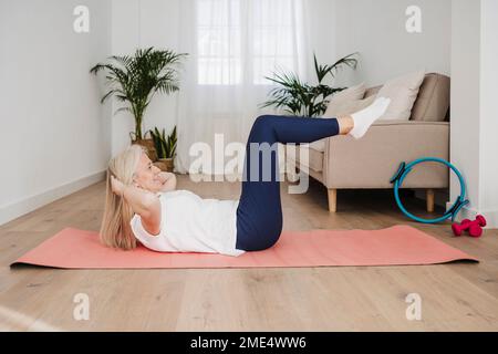 Donna matura che fa sit-up sul tappeto a casa Foto Stock