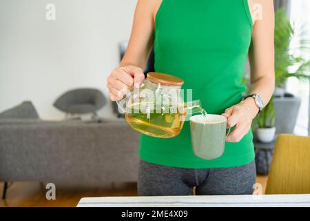 Donna che versa il tè in tazza a casa Foto Stock