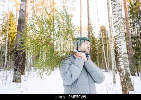 Uomo sorridente che porta l'albero nella foresta invernale Foto Stock