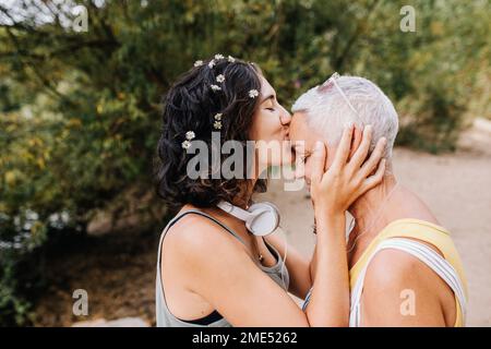 Giovane donna che bacia amico sulla fronte al parco Foto Stock