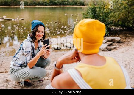 Giovane donna sorridente scattando foto di un amico di fronte al lago Foto Stock