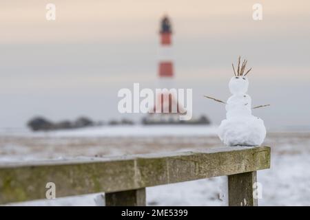 Germania, Schleswig-Holstein, Westerhever, piccolo pupazzo di neve in cima a recinzione di legno con il faro di Westerhoverland sullo sfondo Foto Stock