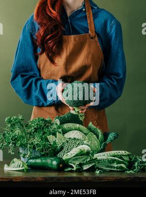 Donna che indossa grembiule che tiene broccoli crudi a tavola Foto Stock