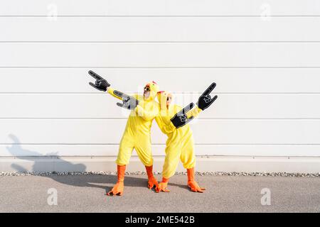 Uomo con donna che indossa costumi di pollo gesturing il giorno di sole Foto Stock